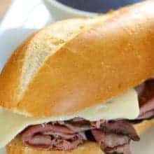 crock pot beef dips sandwich with melty slice of Swiss Cheese and a cup of Au Jus on side