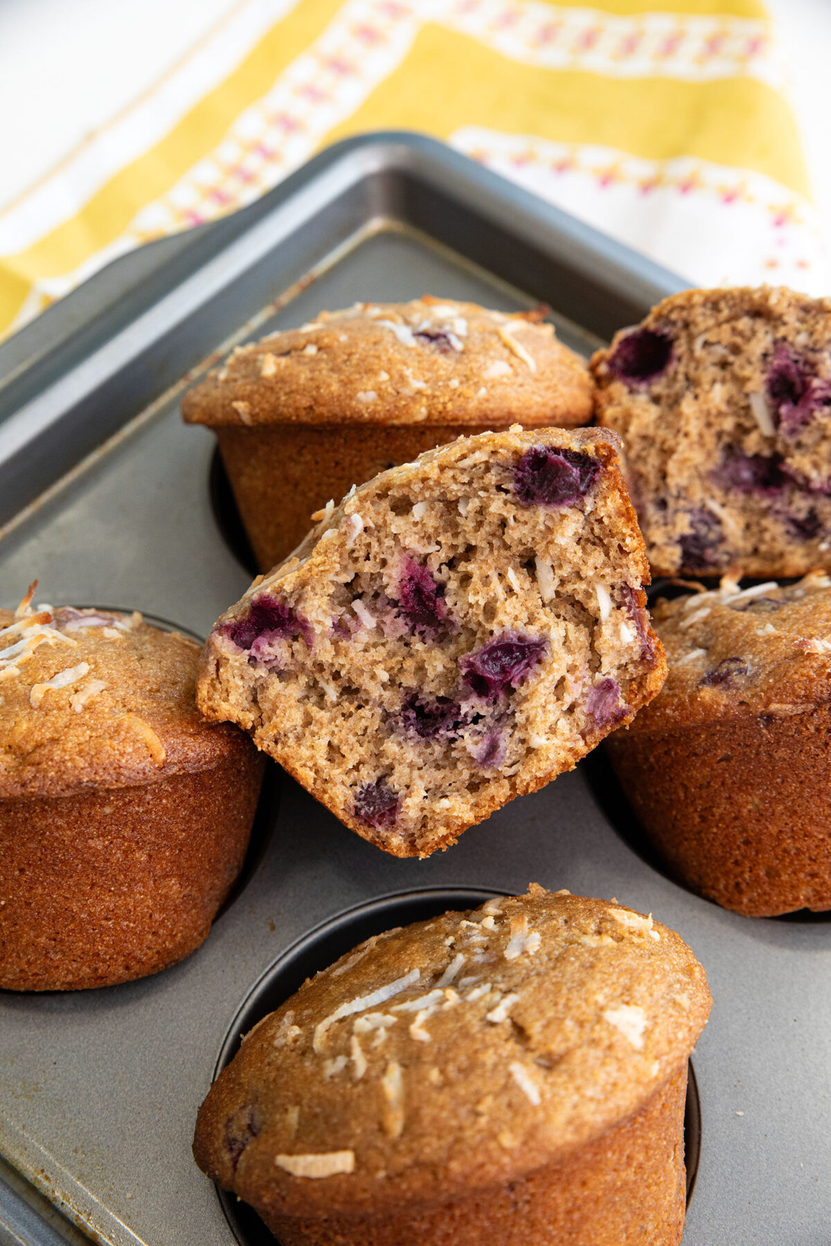close up of a cherry coconut whole wheat muffin cut in half showing cherries inside.