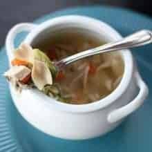 Cheater Chicken Soup in a white bowl with handle, a spoon with vegetables and chopped chicken on top of the bowl