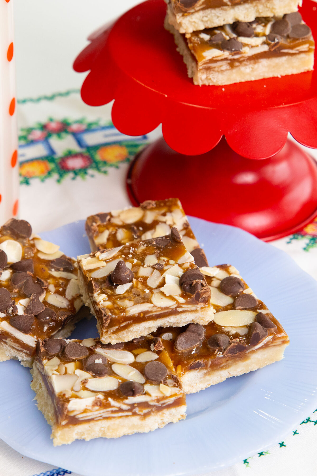 almond crunch toffee bars sliced into squares on a blue plate and ona red cake stand.