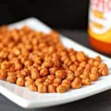 Roasted Chickpeas in a white rectangular plate and a bottle of Buffalo Hot Sauce