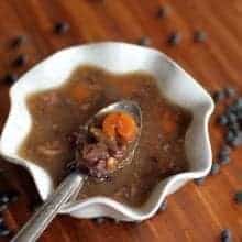 close up of Black Bean & Ham Soup in a White Ruffle Bowl with Spoon, some black beans on background