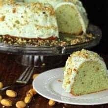 Close up of Homemade Pistachio Pudding Cake with Pistachio Buttercream Frosting in transparent cake holder and a slice in white plate