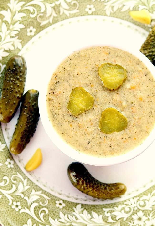 Dill Pickle Soup w małym białym okrągłym naczyniu do pieczenia z kilkoma piklami koperku wokół białego talerza gotowy, aby cieszyć się!