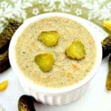 close up shot of Dill Pickle Soup in a small white round baking dish with some dill pickles around a white plate