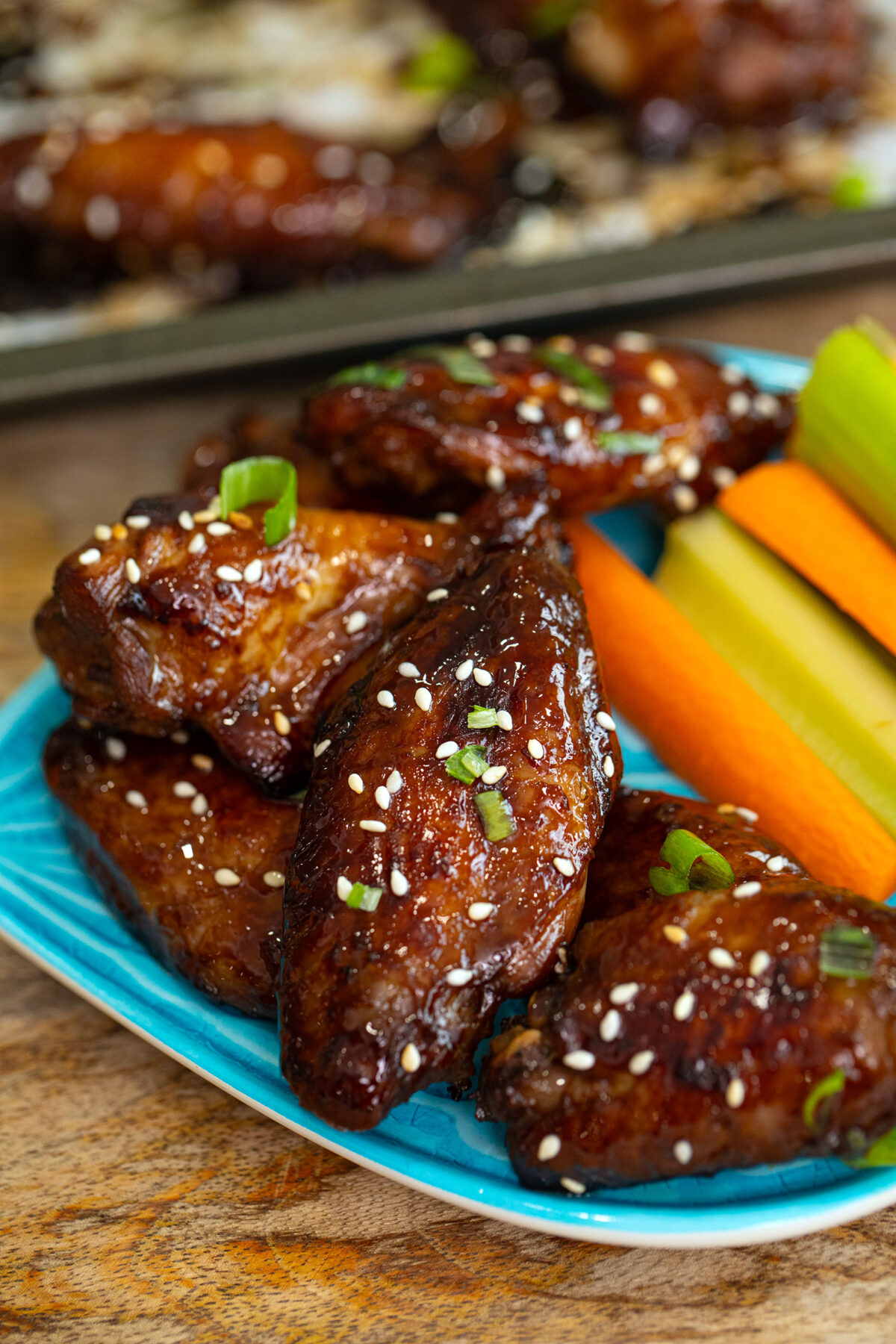 sticky honey wings on a blue plate with carrot and celery sticks