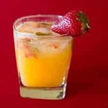 Close up of Short Glass with Tangerine & Gin Garnish with a Piece of Fresh Strawberry on Red Background