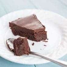 a spoon with Chocolate cake and a slice of Flourless Chocolate Cake in a white plate