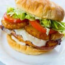 white plate with a Teriyaki Chicken Burger loaded with fillet, pineapple slices, Swiss cheese, tomato slices and shredded lettuce