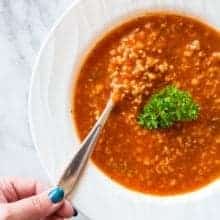 spooning some Tomato & Rice Hamburger Soup in a white plate