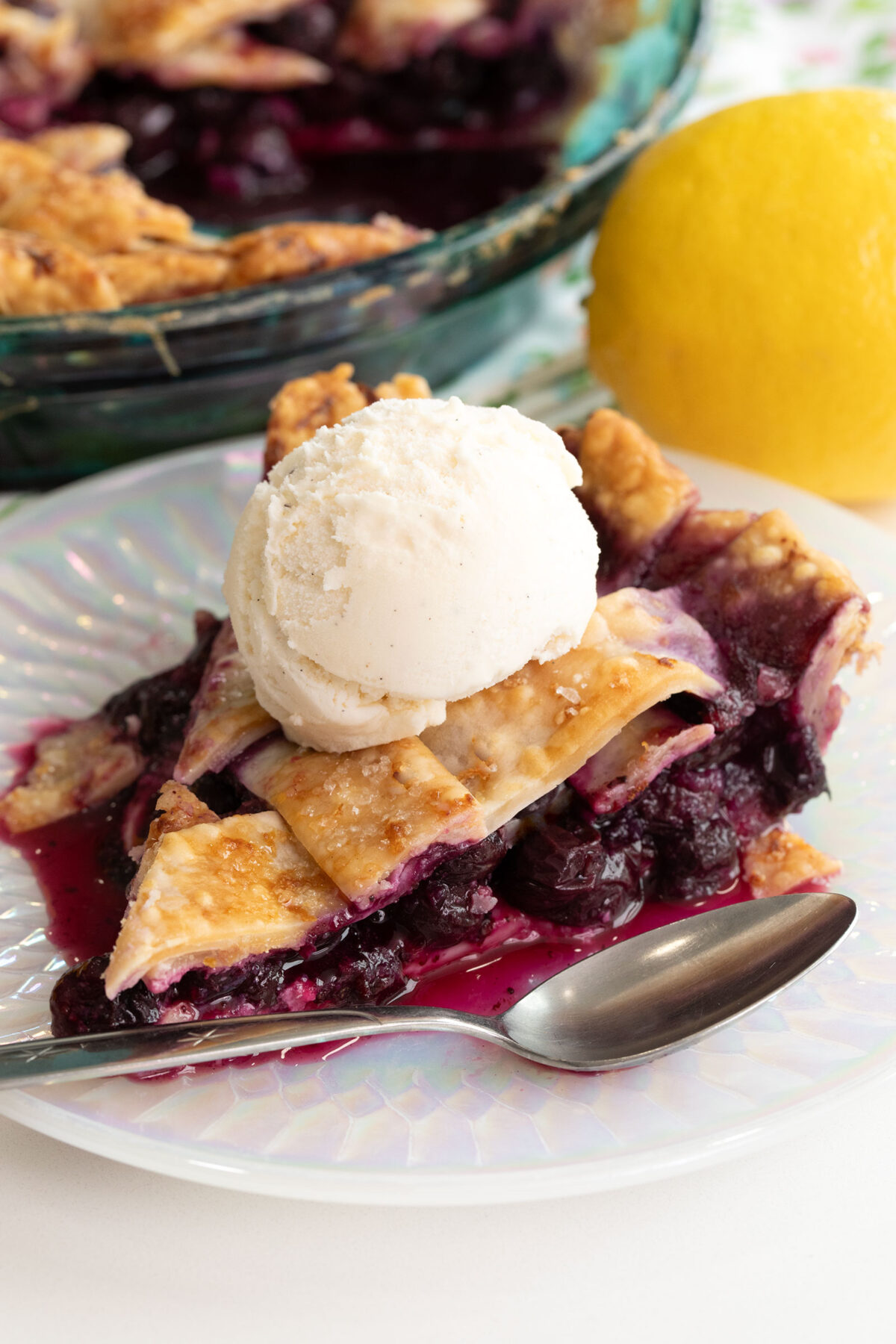 a slice of Lemon blueberry pie on a white plate with a scoop of vanilla ice cream on top.