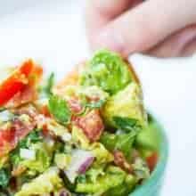 close up hand dipping chips into guacamole in a blue bowl