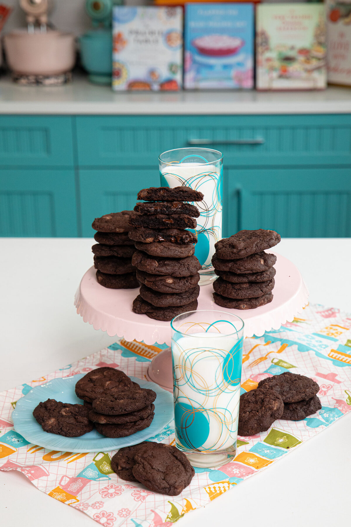 Dark Chocolate Cookies on a blue plate and on a light pink cake stand with a glass of milk.