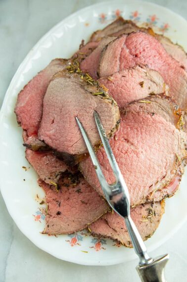 thin slices of stuffed eye of round roast in a white plate with pot fork
