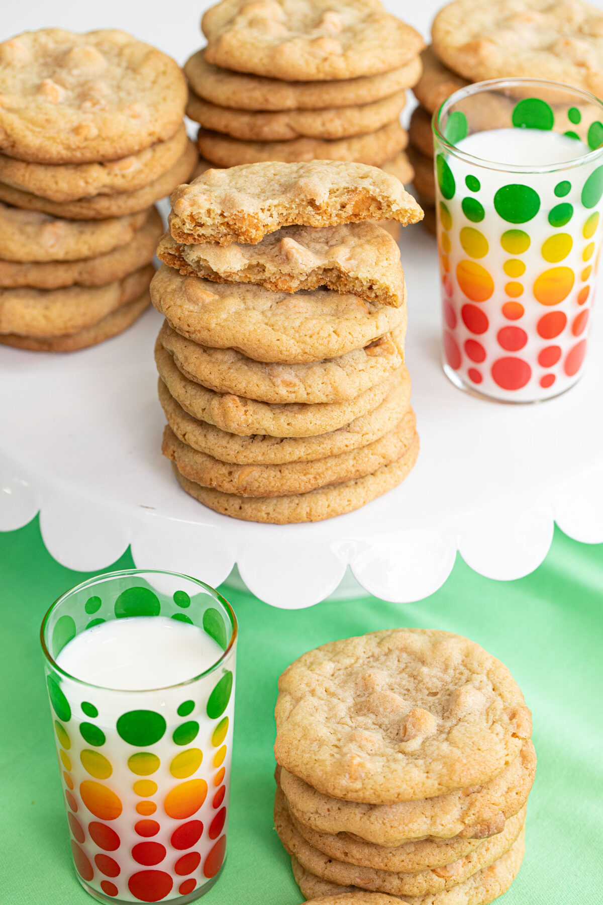 close up of butterscotch cookies in stacks with a glass of milk on a green tablecloth