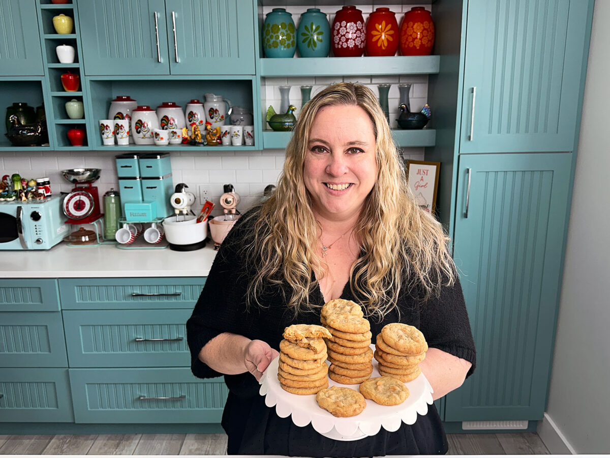 butterscotch cookies in stacks on a white cake stand with karlynn holding them in her kitchen. 
