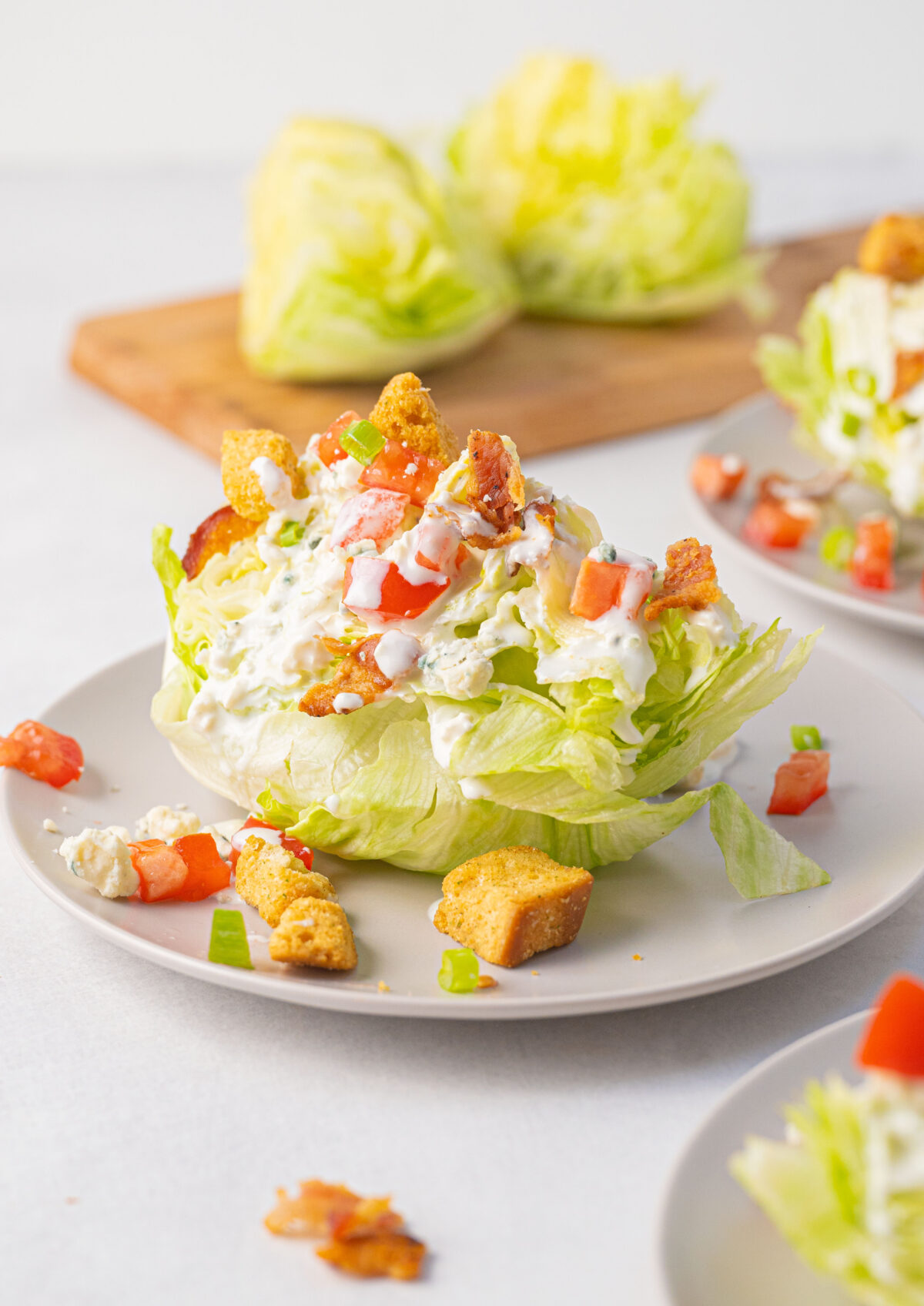 Lettuce wedge on a plate topped with dressing and tomato, bacon and croutons