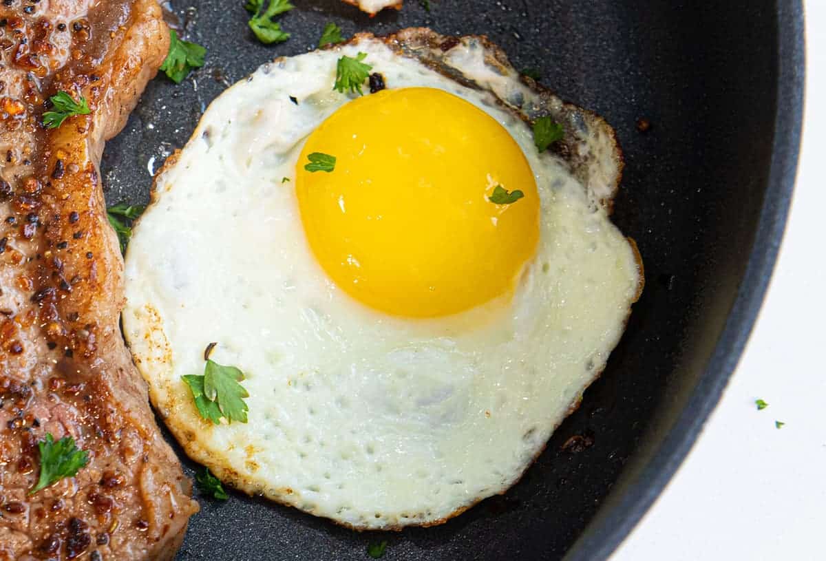 A close-up of a sunny side up fried egg, with flecked bits of parsley dotting the surface.