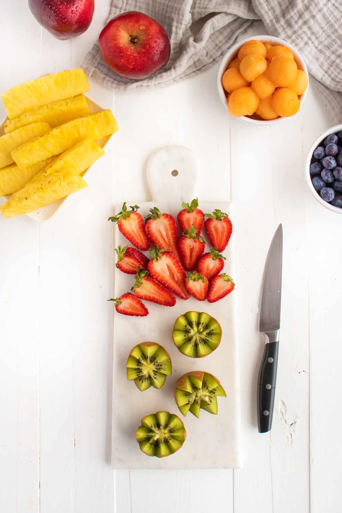 strawberries and kiwis with a knife on a white board