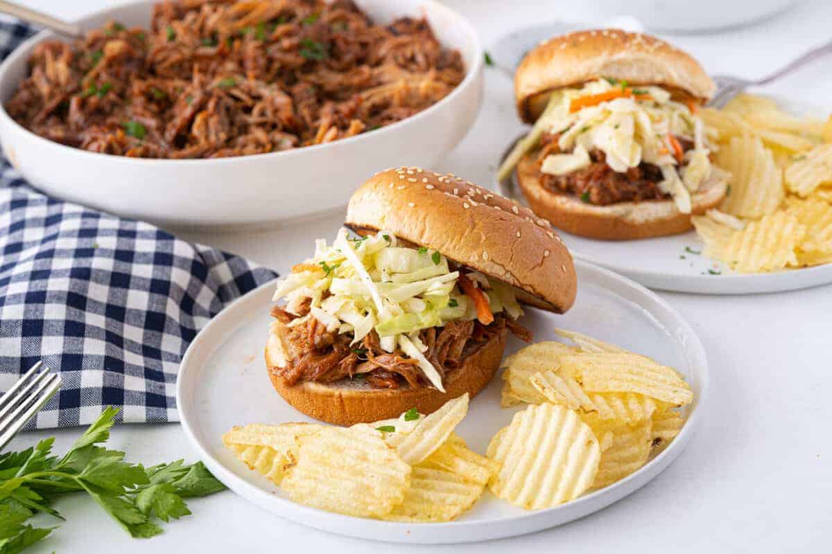 pulled pork sandwiches on a white plate with potato chips 