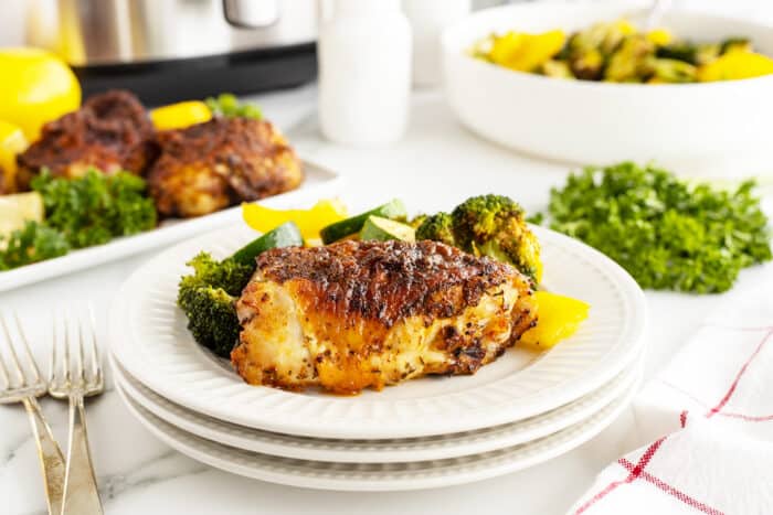 Air fryer chicken thighs on a stack of white plates with broccoli