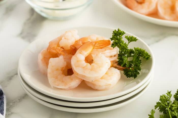 poached shrimp on a stack of white plates with parsley garnish