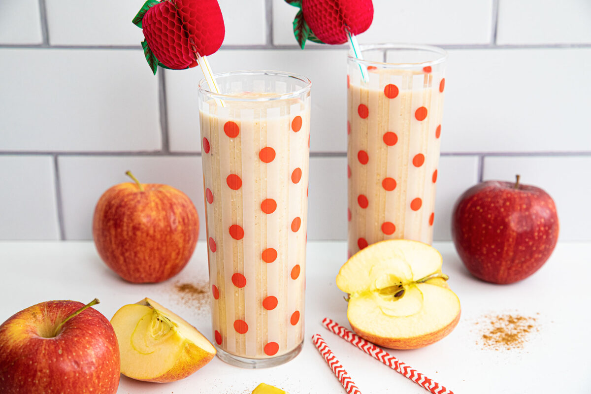Apple smoothies in red dot glasses surrounded by sliced apples and cinnamon