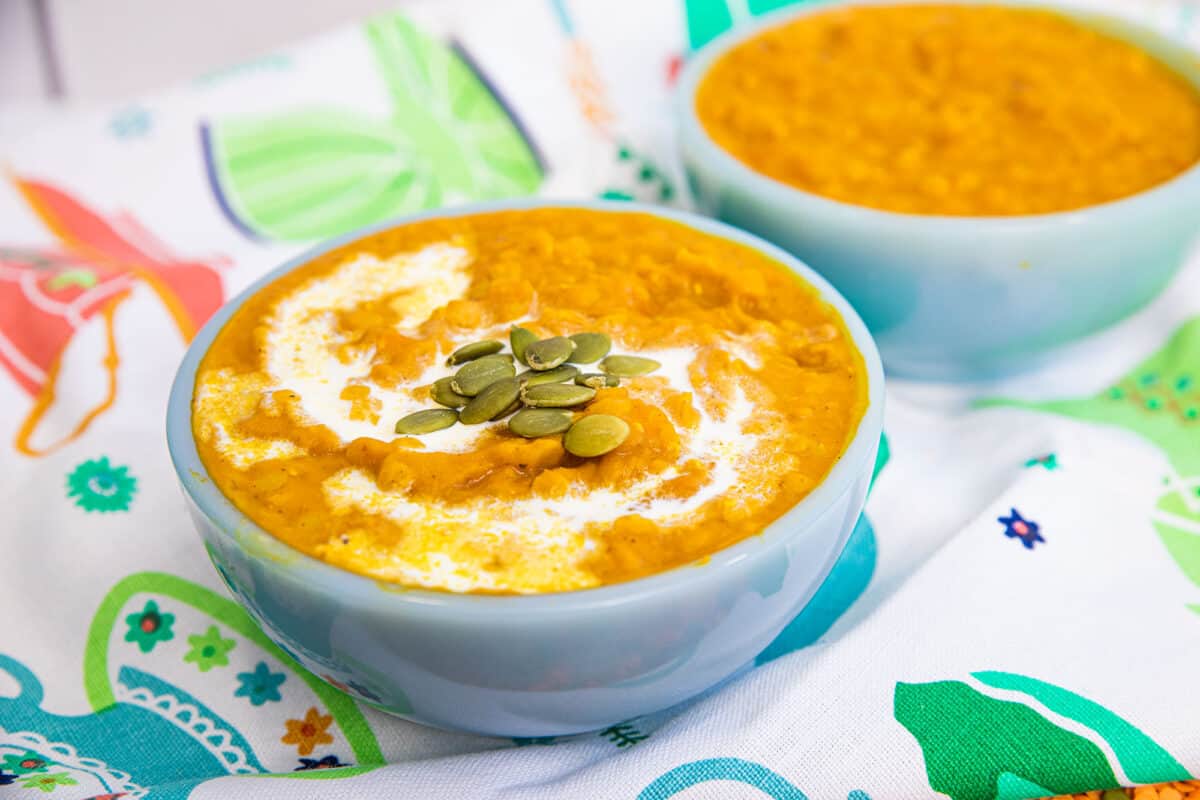 pumpkin lentil soup in a blue bowl with a swirl of cream and pumpkin seeds on top