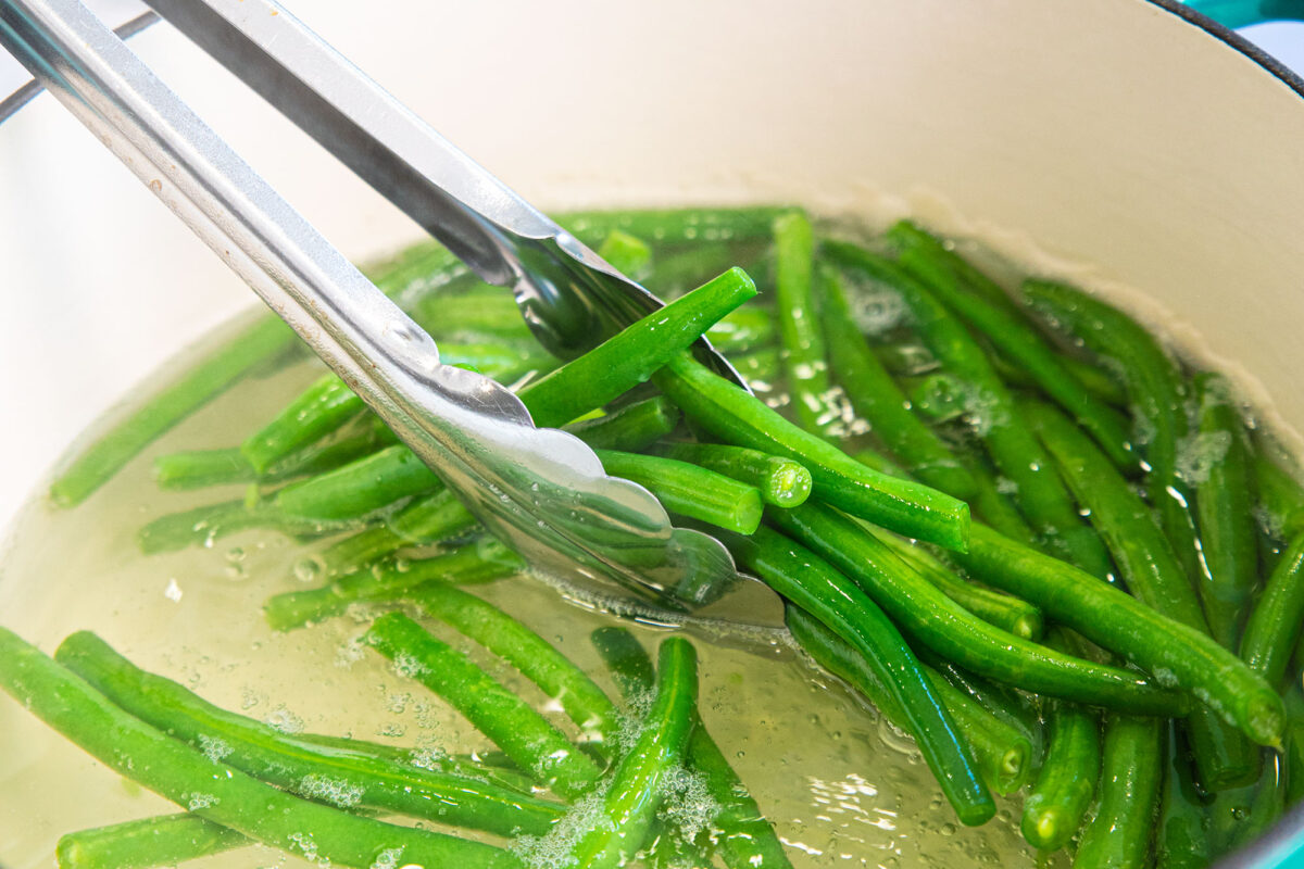 Green beans in a pair of tongs over boiling water