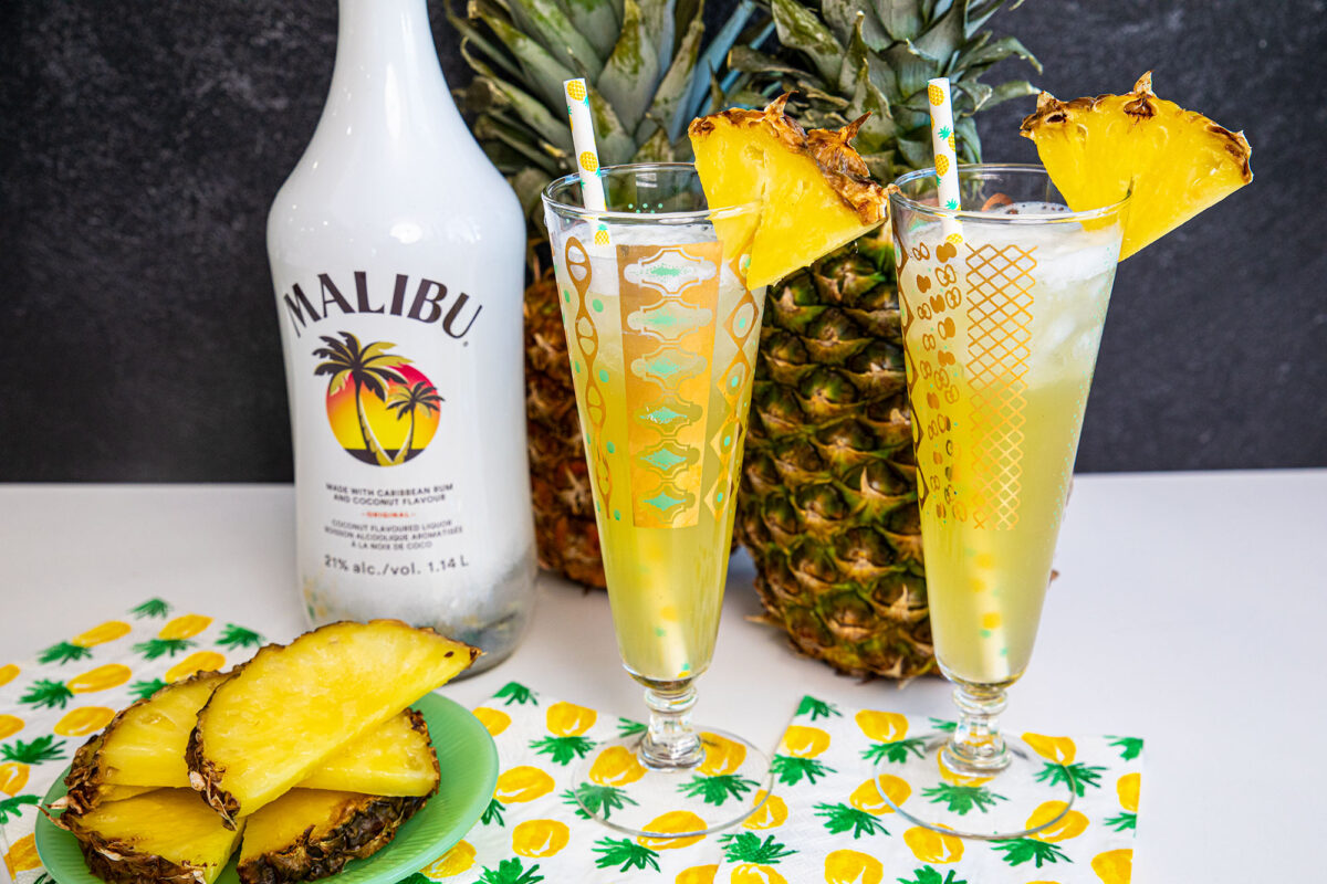 Malibu and Pineapple cocktails on a counter with pineapples in the back ground