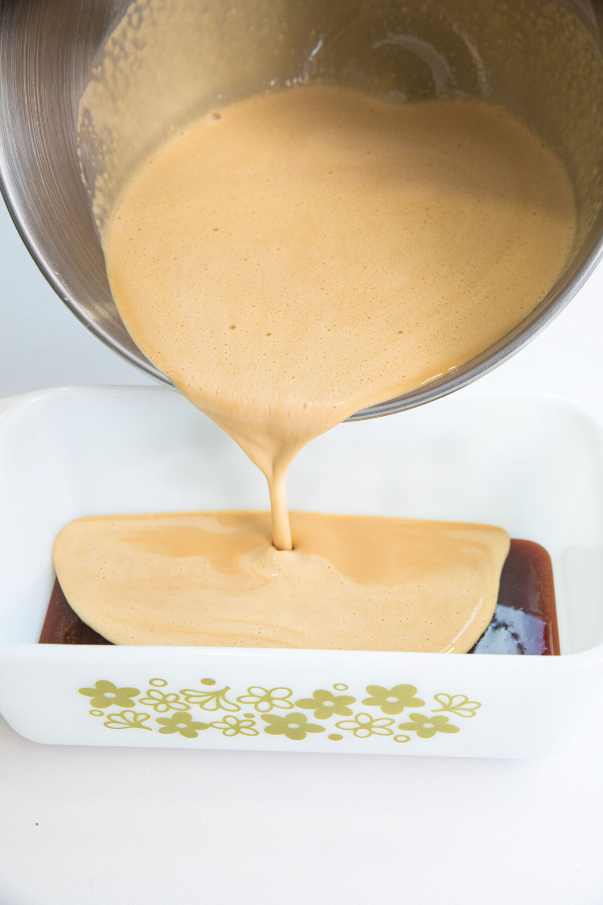 pouring flan batter into the sugar syrup in a loaf  pan