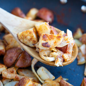 crispy pan fried potatoes and onions with paprika in a medium sized skillet with wooden spoon