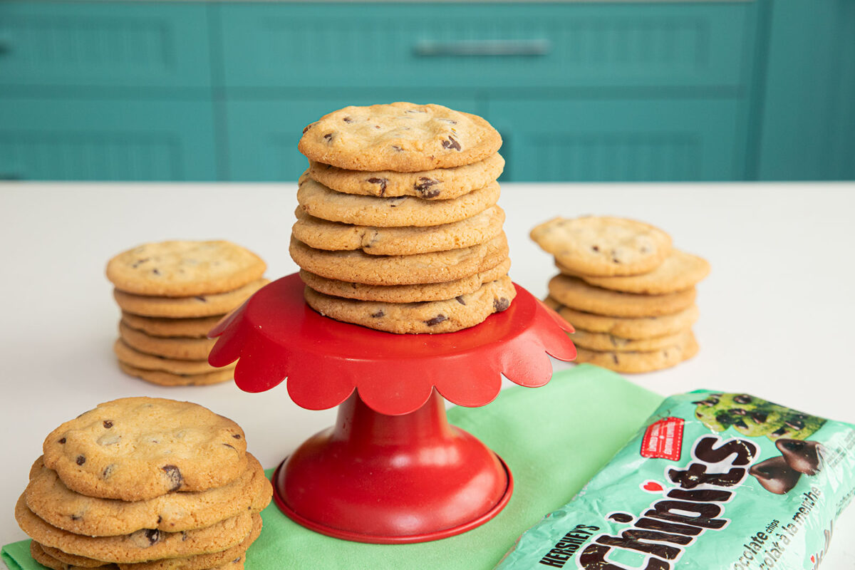 a stack of 7 crispy mint chocolate cookies on a red cake stand with a empty bag of mint chocolate chips at the bottom and stacks of cookies surrounding it.