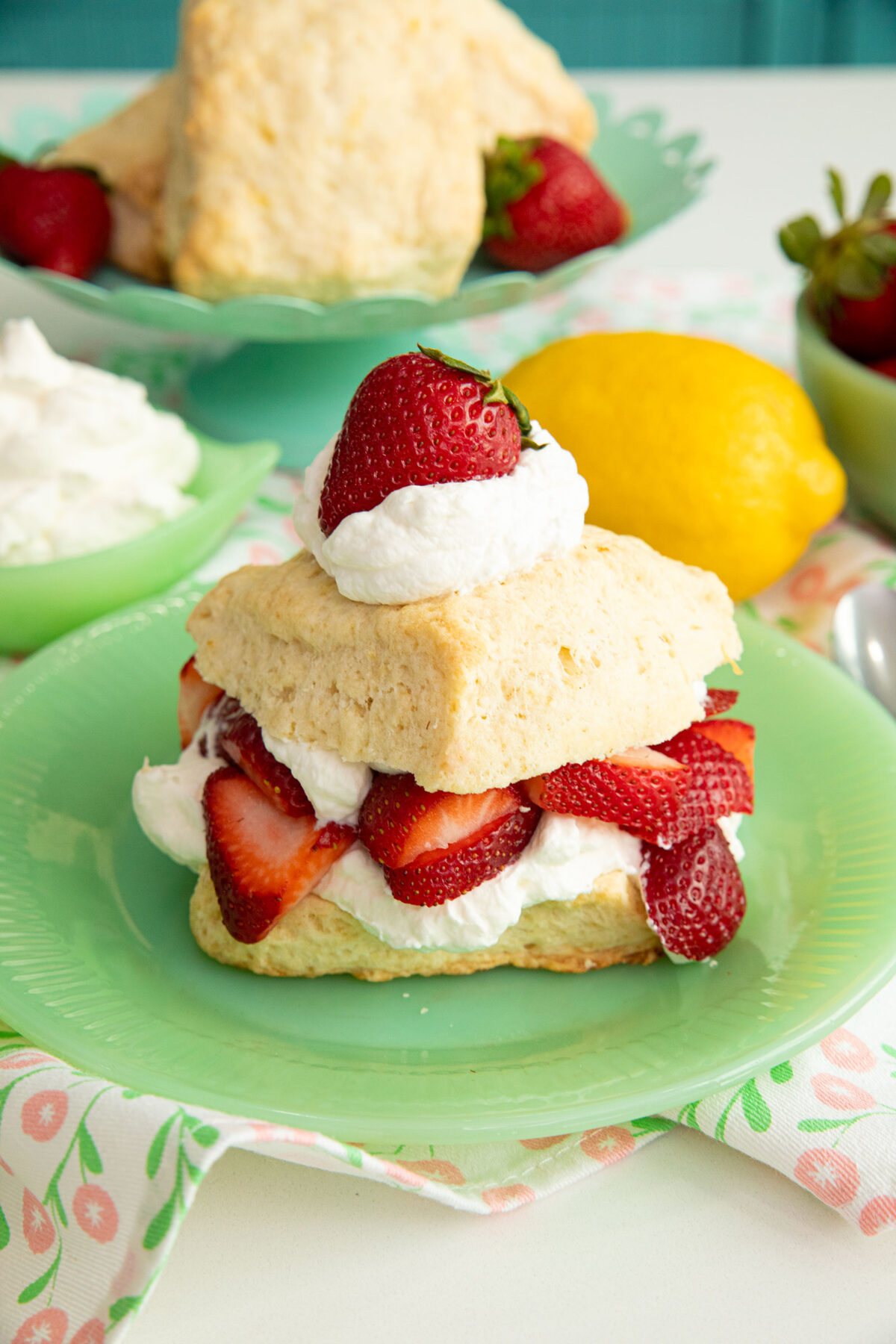 Lemon Strawberry Shortcake on a green plate with a spoonful of topping on top with a whole strawberry on top.