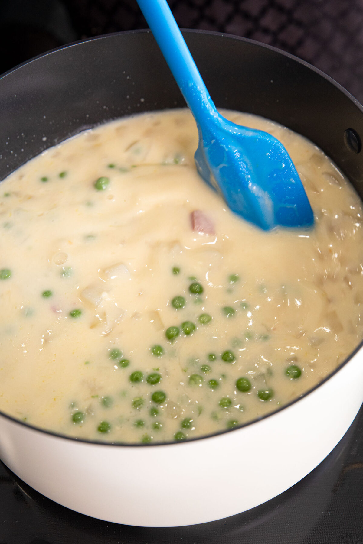 stirring in the green peas into the ham and potato soup