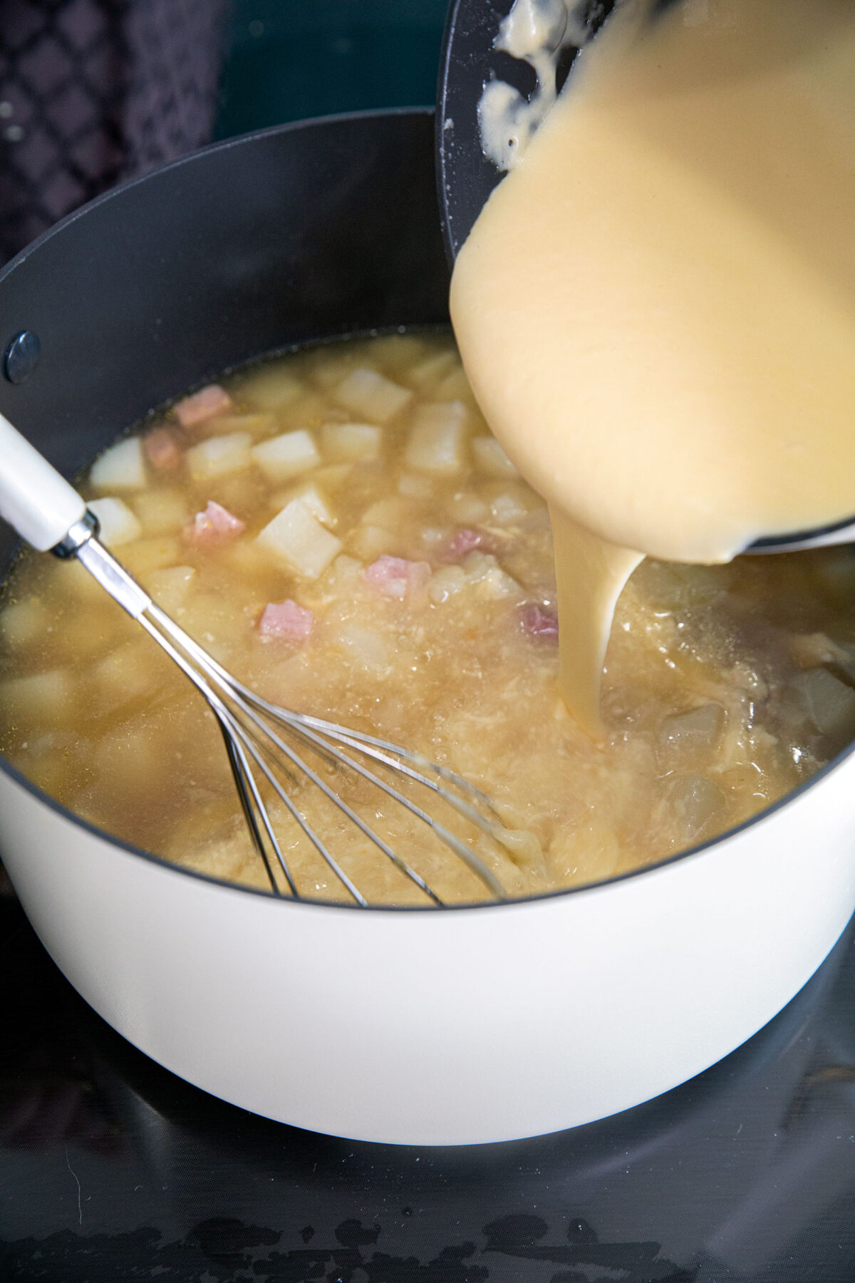 Whisking the roux into the ham and potato soup
