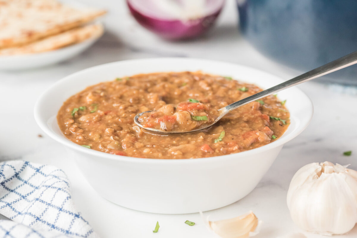 spicy bean and lentil soup in a white bowl with a spoon in in the soup
