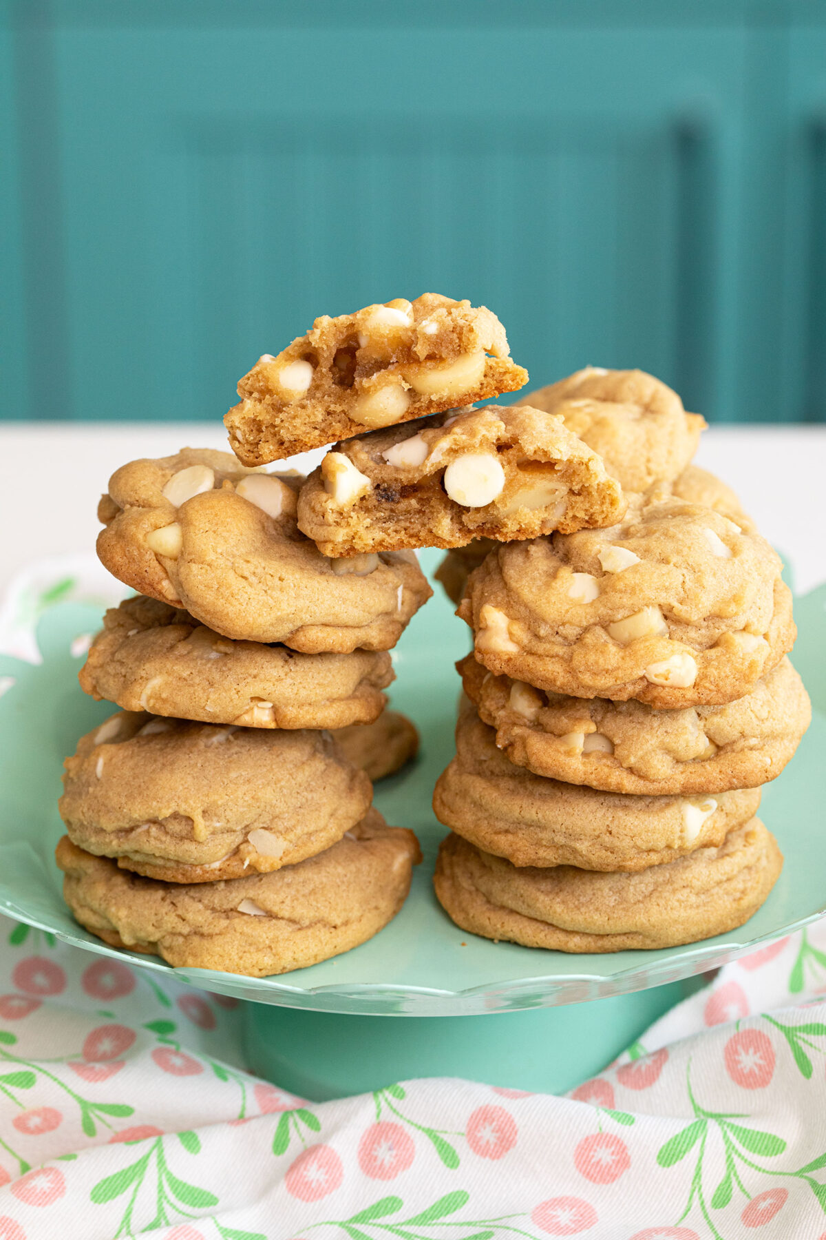 white chocolate chip macadamia nut cookies stacked with a cookie broken in half showing the inside.