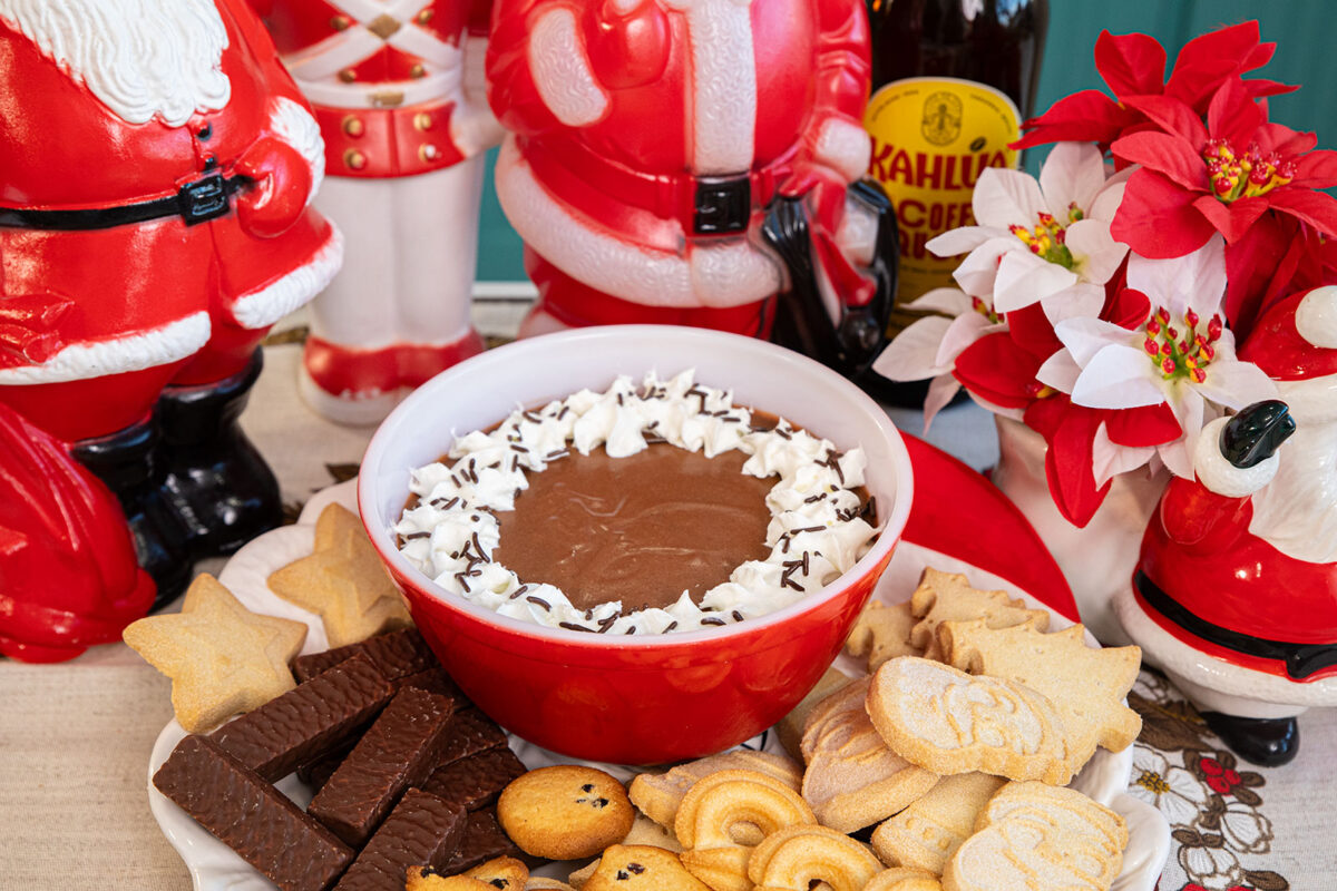 Kahlua cheesecake dip in a bowl on a table surrounded by cookies and snacks.